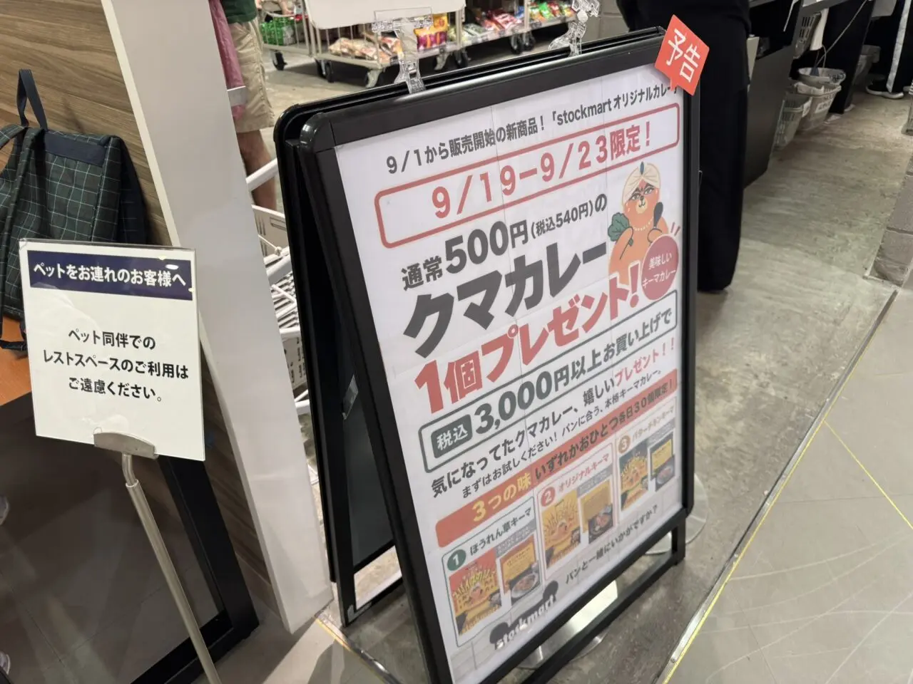 stockmart入口前に設置されたクマカレープレゼントの案内看板と買い物かご