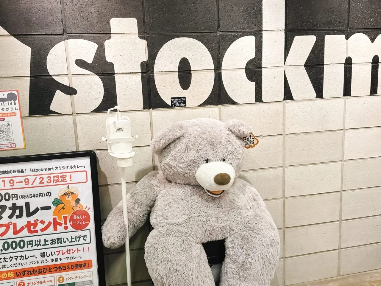 stockmartのロゴが壁に描かれた通路に置かれた大きなクマのぬいぐるみと告知看板