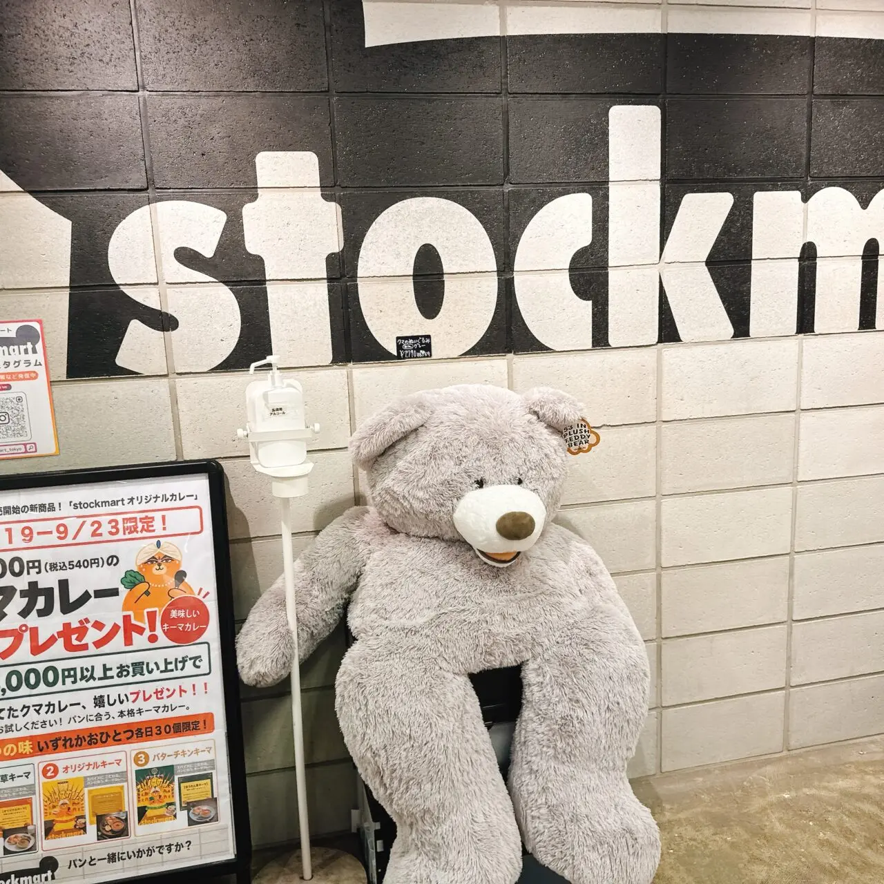 stockmartのロゴが壁に描かれた通路に置かれた大きなクマのぬいぐるみと告知看板