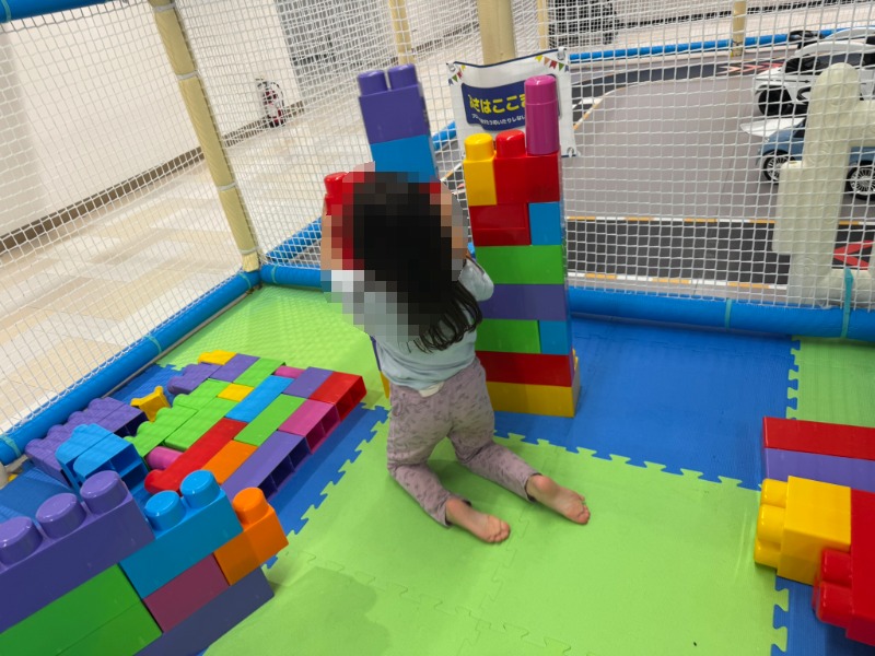 マット敷きのスペースでカラフルな大型ブロックを組み立てる子ども