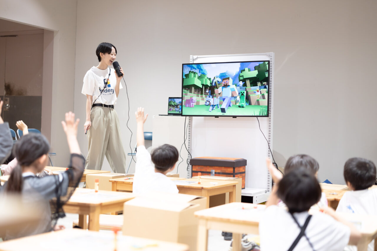 モニター画面のマイクラ映像を見ながら元素の解説を聞く小学生たち