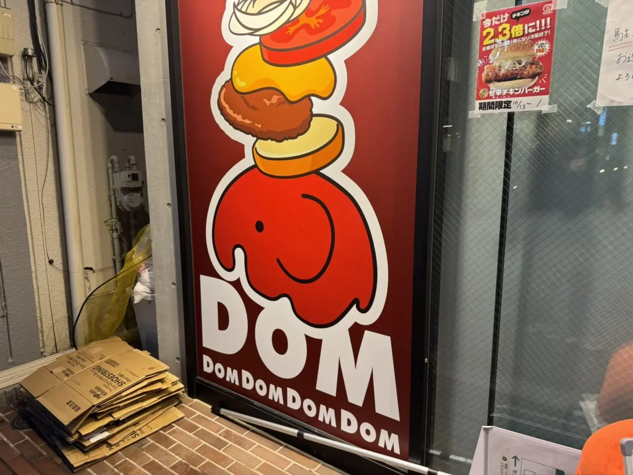 ドムドムハンバーガーのシンボル「どむぞうくん」の頭の上にバンズやパティが乗った大きな赤い看板