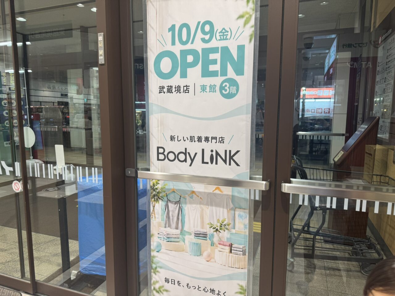 店舗のガラスドアに貼られた「10/9(金) OPEN 新しい肌着専門店 Body LiNK 武蔵境店 東館3階」の縦長オープンポスター
