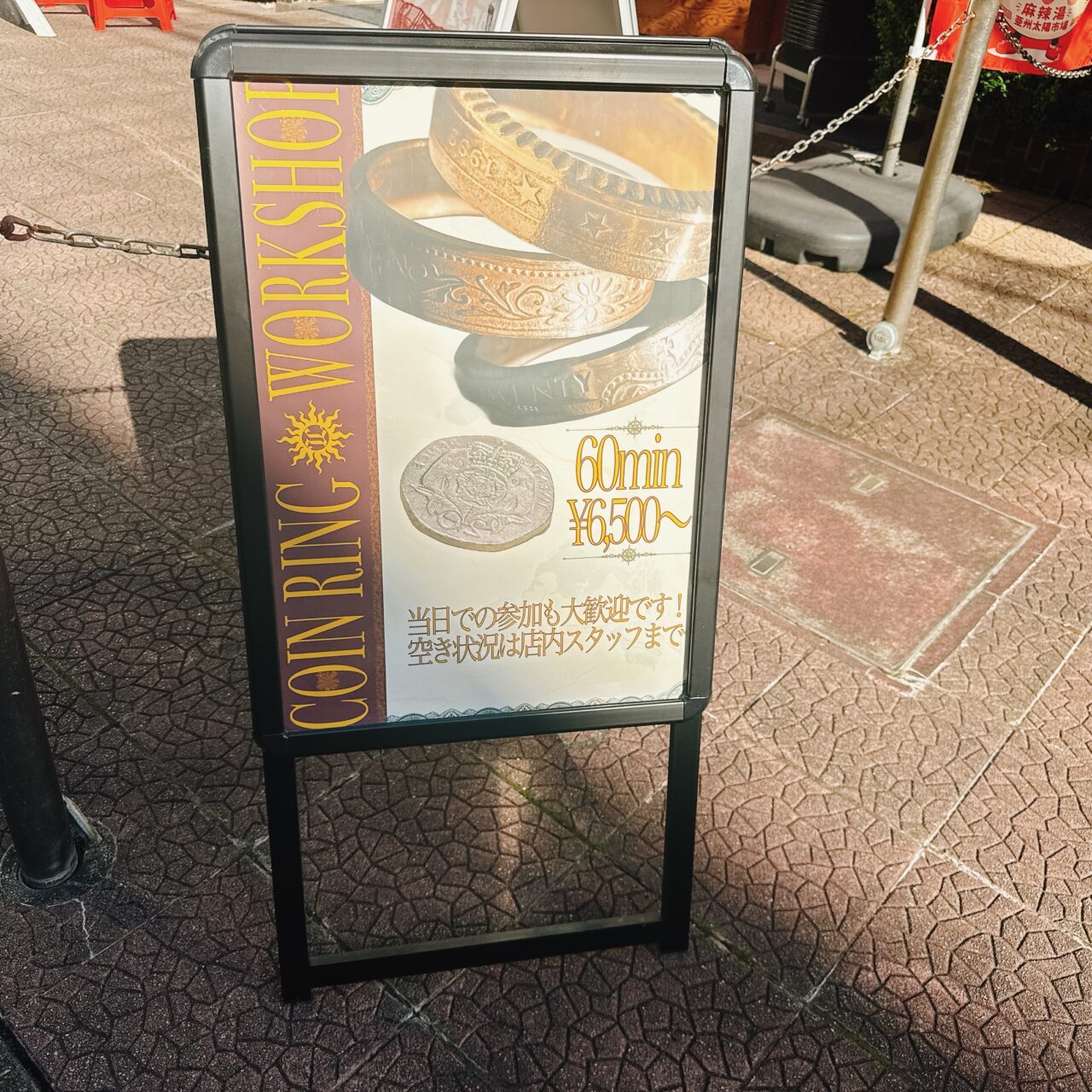 「COIN RING WORKSHOP 60min ¥6,500〜」と書かれたコインリング体験の店頭スタンド看板。精密な模様が刻まれた指輪の写真