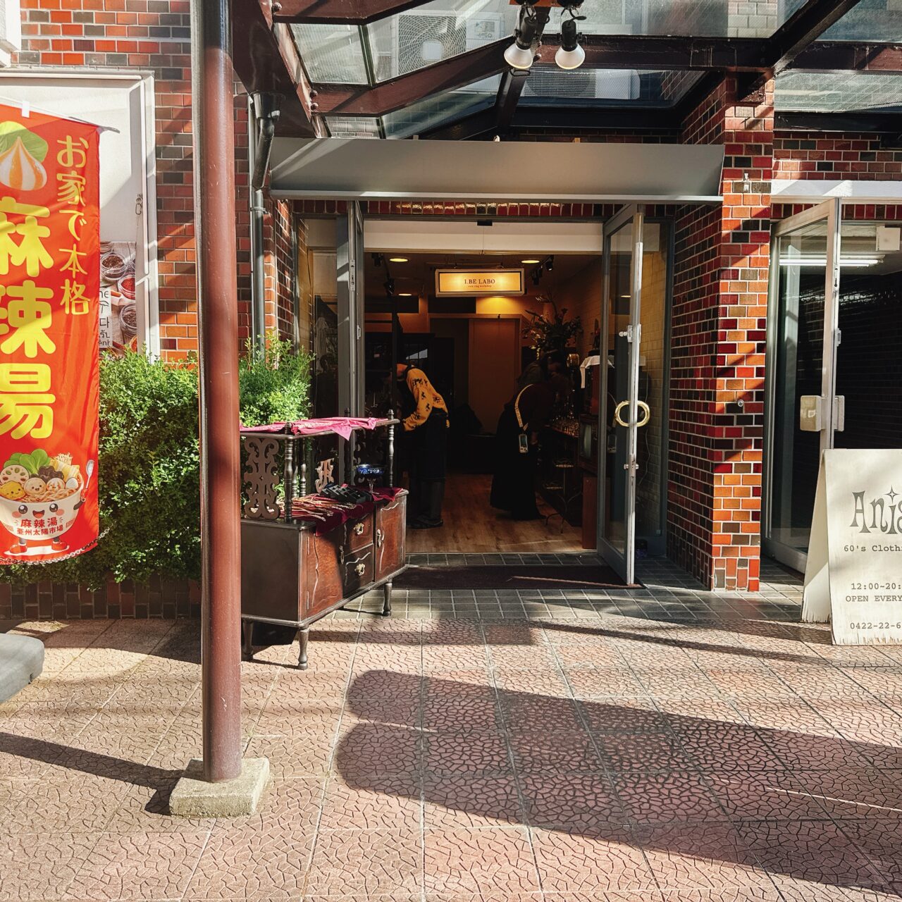 レンガ調のエントランスと「I BE LABO」の看板が灯る店舗外観。アンティーク調のチェストが置かれた店先