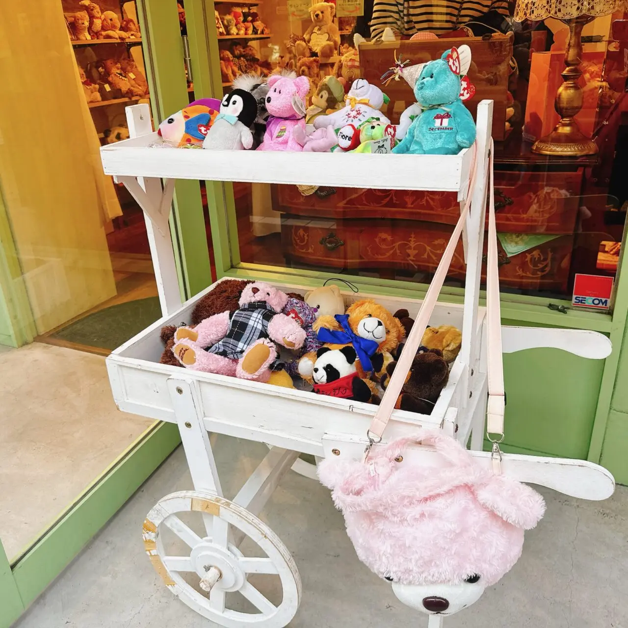 店先に置かれた白い木製カートワゴン。ピンクのくまやカラフルなぬいぐるみが詰められている様子