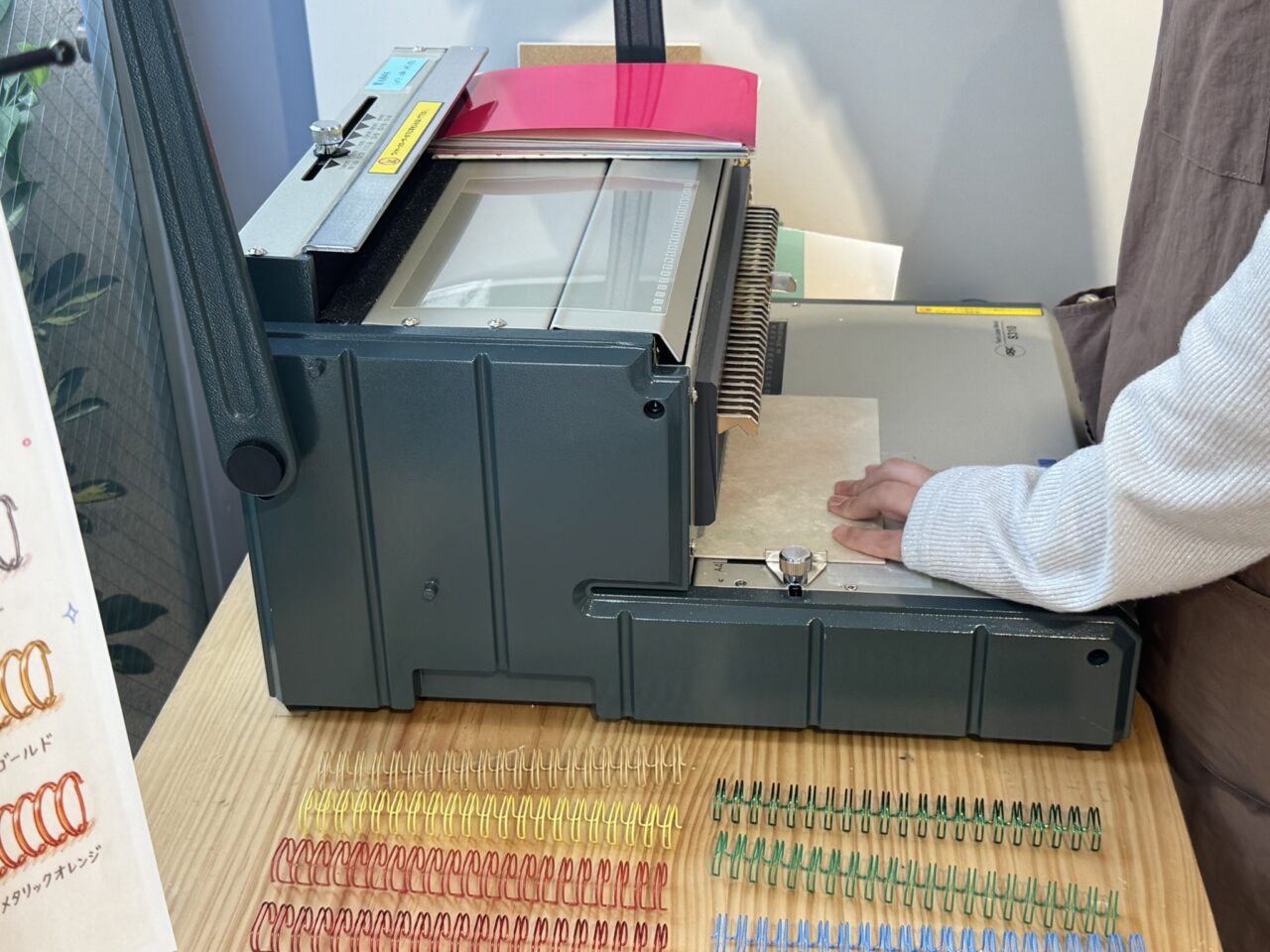 スタッフが卓上製本機を使ってノート用紙に穴を開けリングを通す製本作業の様子