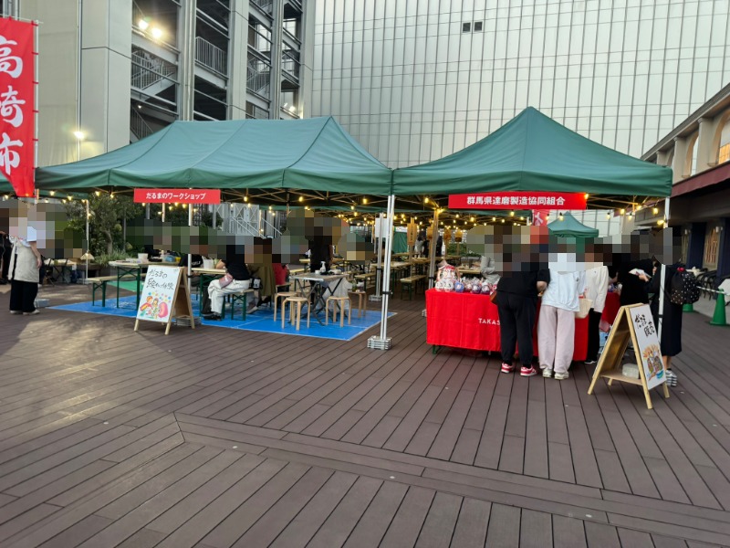 屋上広場のウッドデッキに並ぶキッチンカーとワークショップのテント、高崎市の赤い旗がはためく様子