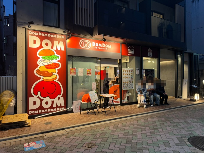 ドムドムハンバーガー吉祥寺FC店の店舗外観。大きなどむぞうくんの看板と、店先のベンチで入店を待つお客さんたちの様子